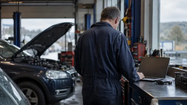 A garage owner in Livingston sits beside vehicle keys with a laptop open and its screen turned away from the camera.