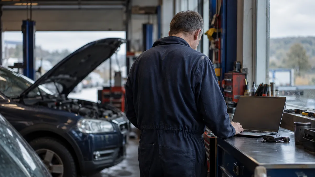 A garage owner in Livingston sits beside vehicle keys with a laptop open and its screen turned away from the camera.