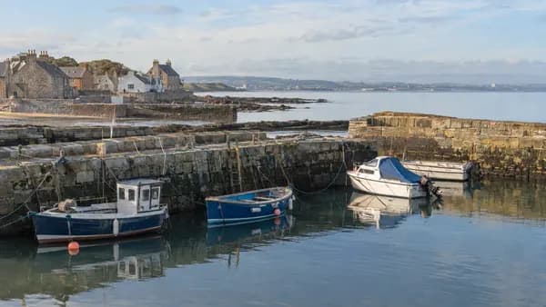 A small harbour with fishing boats and pleasure craft moored against a stone wall on a bright morning on the East Lothian coast.