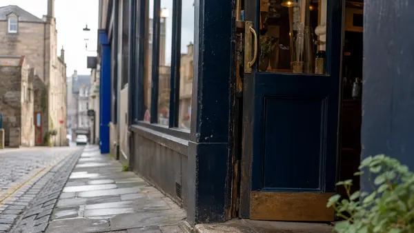 A shop doorway on a Scottish high street with the open sign showing and the door propped ajar.