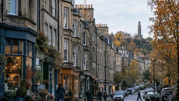 A quiet shopping street of stone tenements with small independent shopfronts at ground level on a bright autumn morning in Edinburgh.