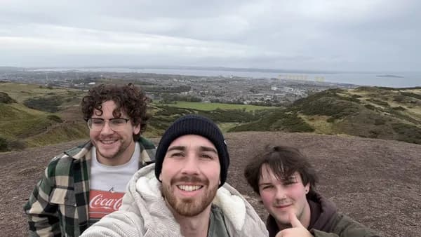 Three people on the top of Arthur's Seat on a grey day, Edinburgh and the Firth of Forth spread out behind them.