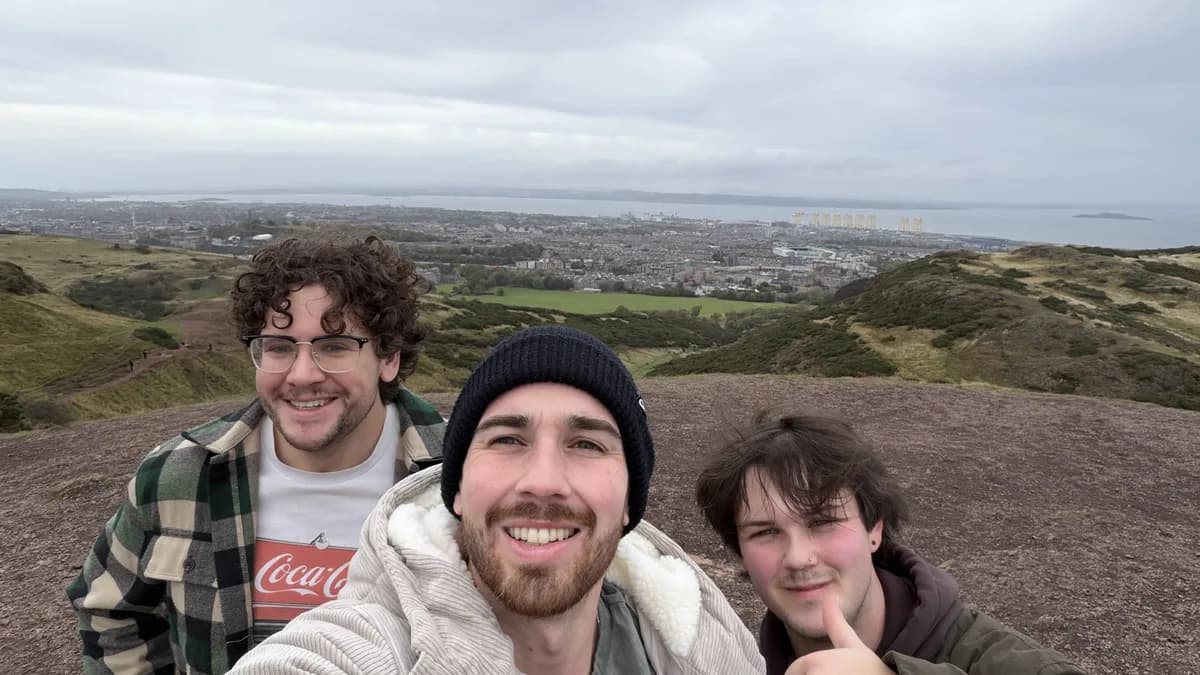 Three people on the top of Arthur's Seat on a grey day, Edinburgh and the Firth of Forth spread out behind them.